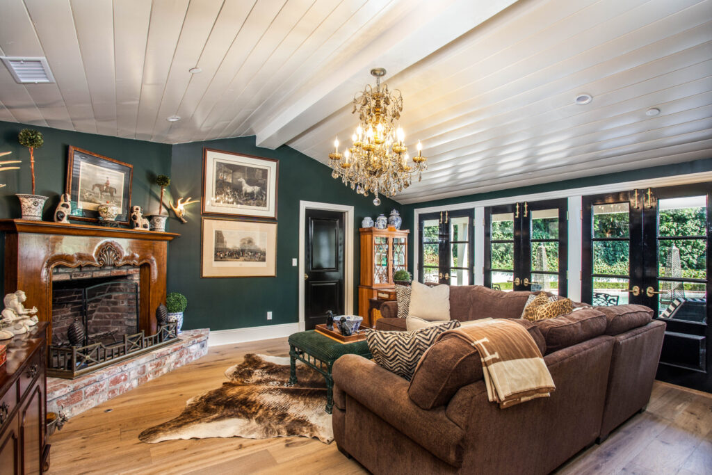 home builders Cozy living room with brown sofas, a fireplace, chandelier, and large windows overlooking greenery.
