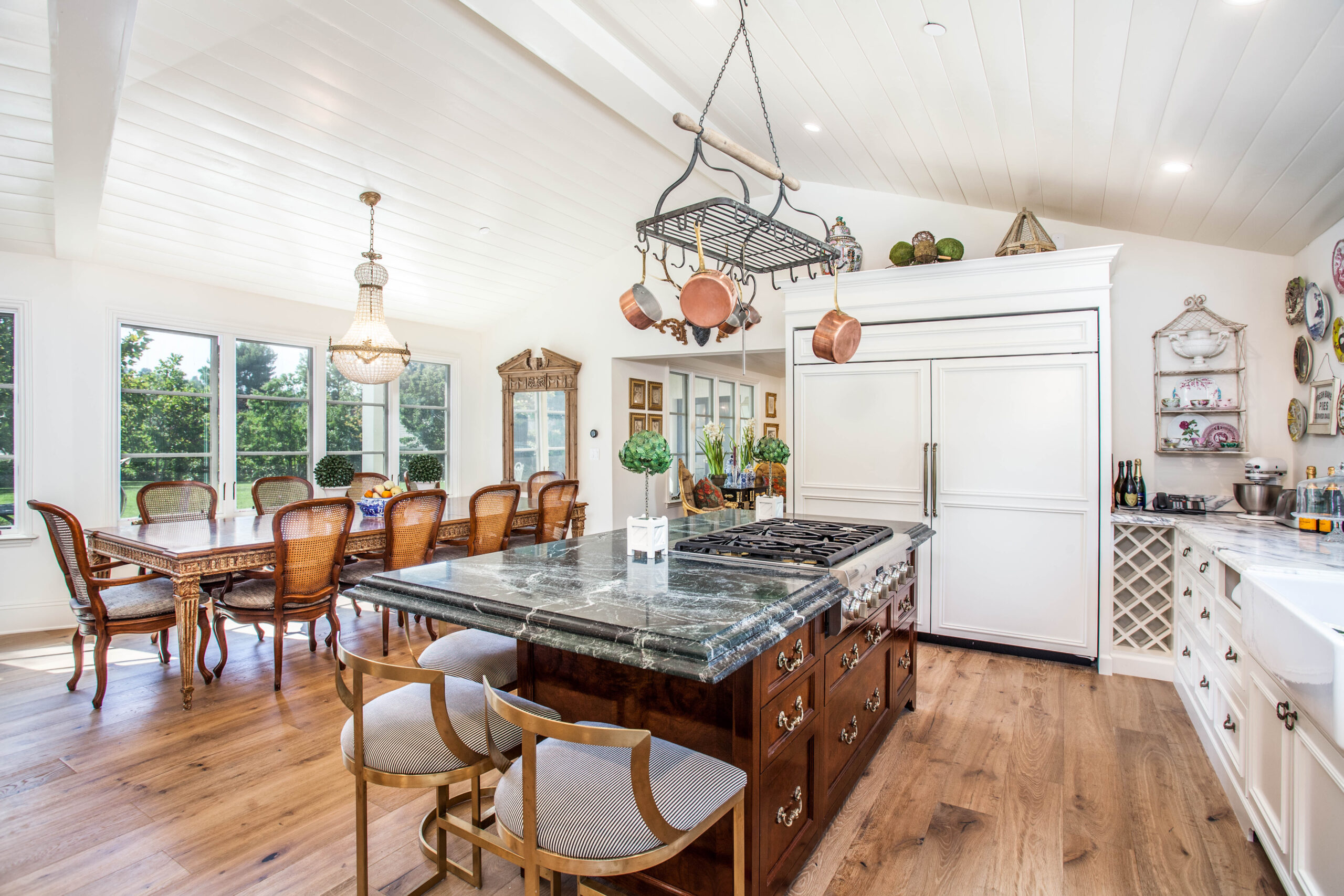 Bright kitchen with a large island, hanging pots, wooden dining table, and elegant decor in a white, airy space.