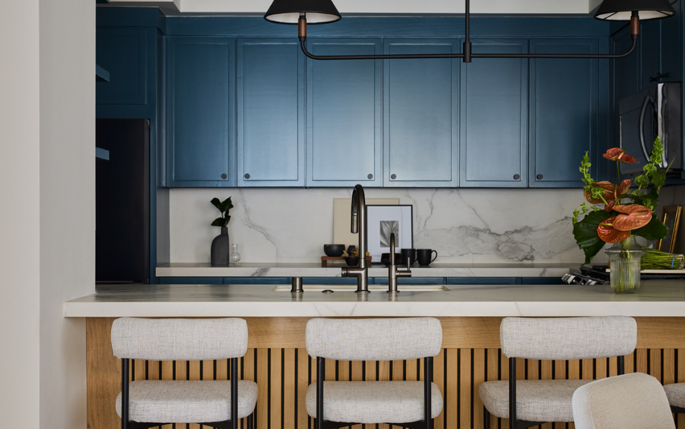 Experience a modern kitchen renovation with blue cabinets, a marble backsplash, and a wooden island adorned with light upholstered stools. Perfect for those considering kitchen remodeling for a stylish upgrade.