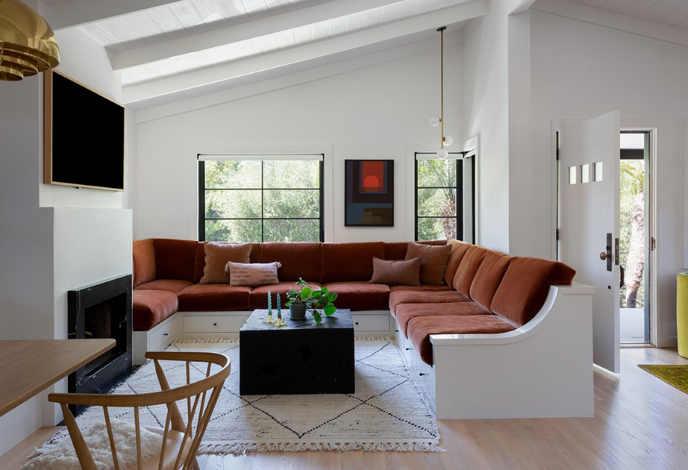 Cozy living room with a large brown sectional sofa, black coffee table, and wall-mounted TV, near windows and open door.