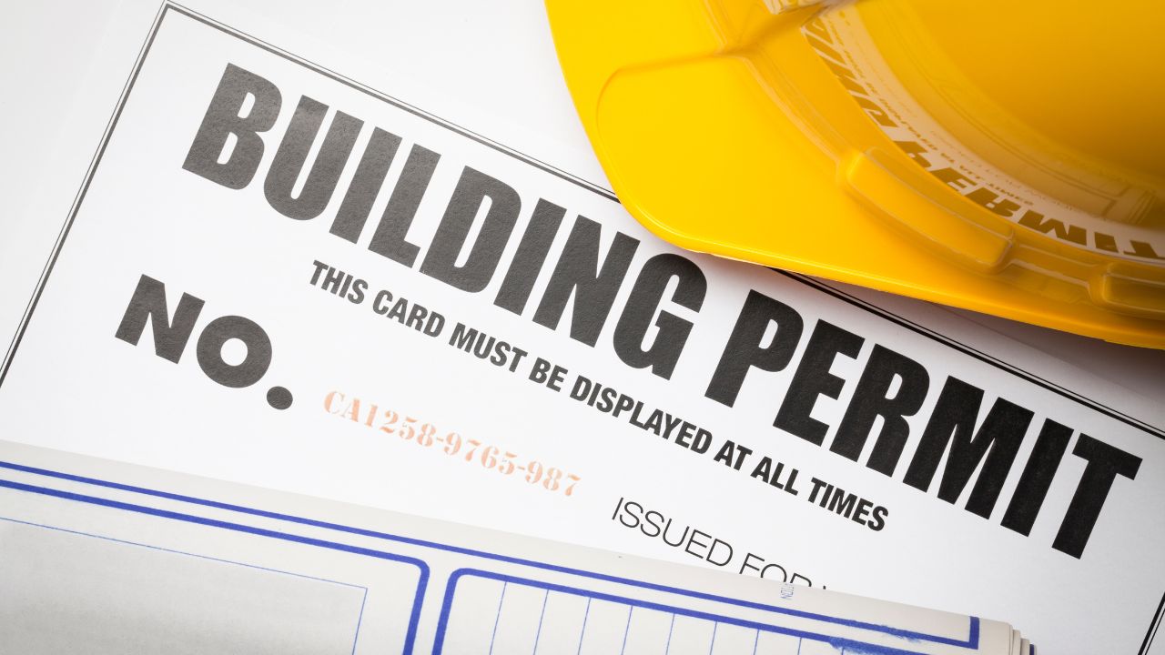 A building permit with a yellow hard hat placed on top, symbolizing the start of a custom home build.